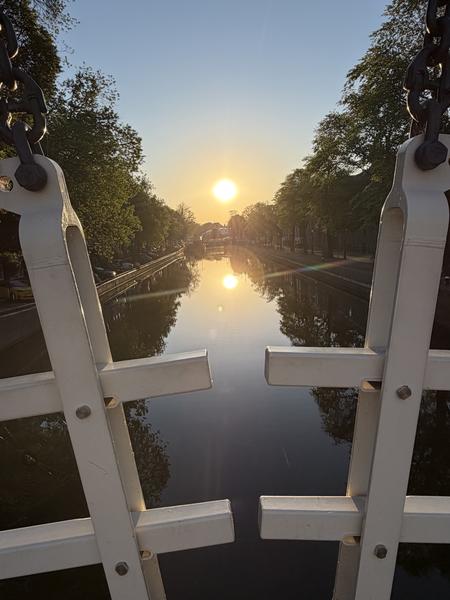 This photo captures a beautiful sunrise over the Amstel canal in Weesperbuurt, Amsterdam, framed by the white structure of a bridge